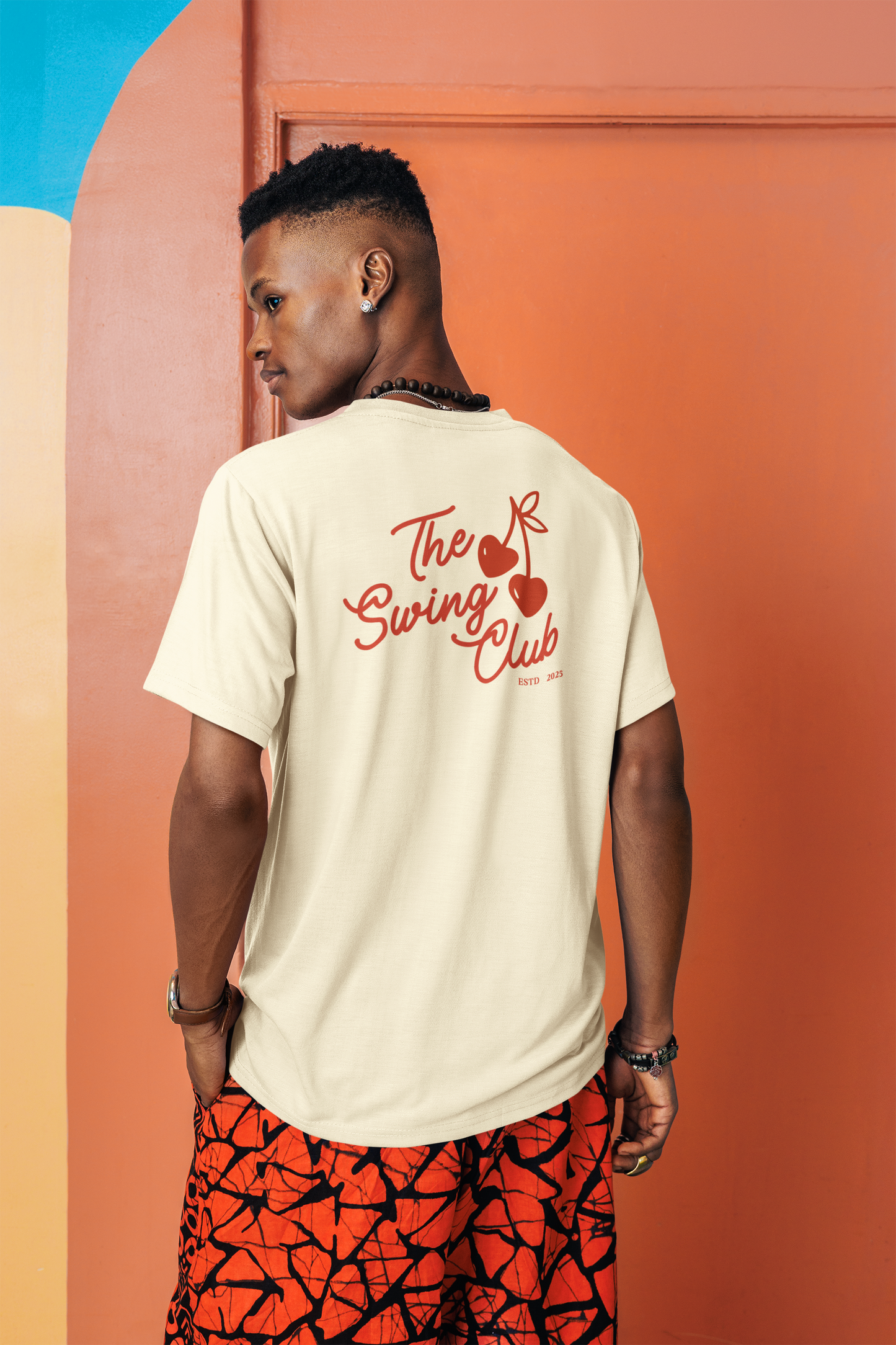 Person wearing a beige t-shirt with 'The Swing Club' design, standing against a colorful background.